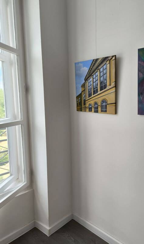 Roh miestnosti s veľkým oknom v Galérii vo veži, v poľovníckom kaštieli Palárikovo a so zaveseným obrazom budovy - priečelia kaštiela, kde sa v oblokoch odrážajú oblaky.